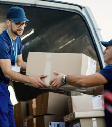 Young couriers cooperating while unloading packages from deliver Delivery men loading carboard boxes in a van while getting ready for the shipment.